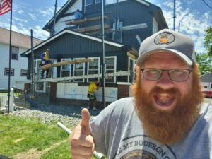 A man with a beard giving a thumbs up in front of a house